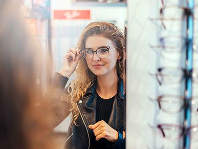Frau im Brillengeschäft probiert vor einem Spiegel eine Brille aus