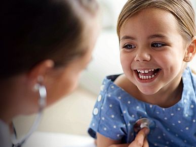 Kleines Mädchen lächelt die Ärztin an, während diese das Kind untersucht