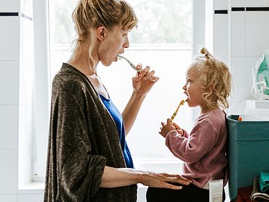 Eine Mutter und ihr Kind putzen sich gemeinsam die Zähne.