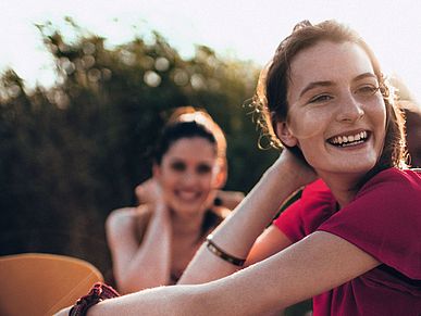 Vier Frauen sitzen fröhlich lächelnd auf einem Feld.