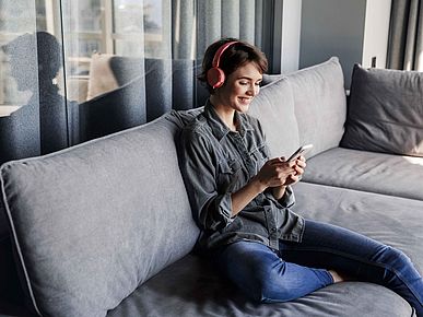 Frau sitzt auf dem Sofa und schaut auf ihr Smartphone