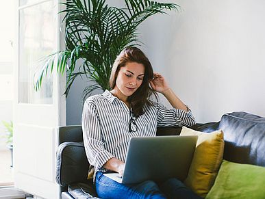 Frau sitz auf dem Sofa mit einem Laptop auf den Beinen.