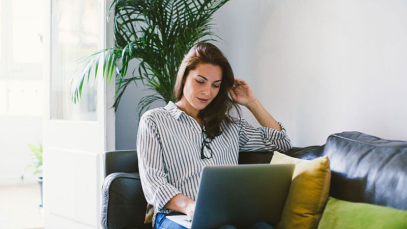 Frau sitz auf dem Sofa mit einem Laptop auf den Beinen.