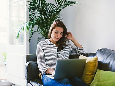 Frau sitz auf dem Sofa mit einem Laptop auf den Beinen.