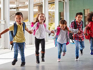 Schulkinder laufen mit Schulranzen über den Schulhof und halten sich dabei an den Händen.