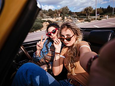 Zwei junge Frauen mit Sonnenbrillen in einem Cabrio