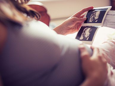 Frau hält ihren Schwangerschaftsbauch und schaut sich Ultraschallbilder an