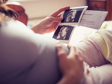 Frau hält ihren Schwangerschaftsbauch und schaut sich Ultraschallbilder an
