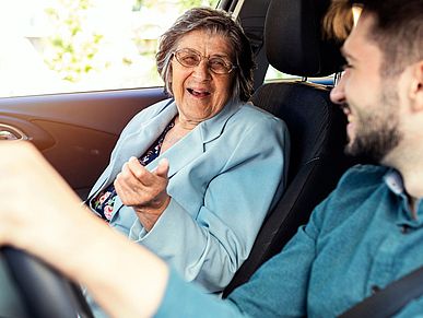 Eine Seniorin und ein junger Mann fahren gemeinsam im Auto.