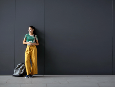 Studentin mit Rucksack vor einer grauen Wand stehend
