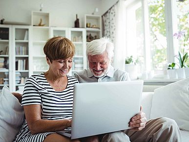 Zwei ältere Menschen sitzen auf dem Sofa und schauen auf einen Laptop