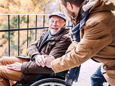 Älterer Herr im Rollstuhl ist mit einem jüngeren Mann auf einem Spaziergang