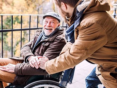 Älterer Herr im Rollstuhl ist mit einem jüngeren Mann auf einem Spaziergang