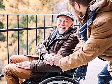 Älterer Herr im Rollstuhl ist mit einem jüngeren Mann auf einem Spaziergang