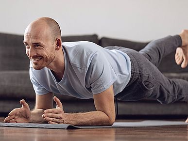 Mann macht eine Fitnessübung im Wohnzimmer und ist fröhlich