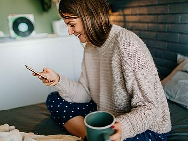 Frau sitz auf ihren Bett und schaut auf ihr Handy