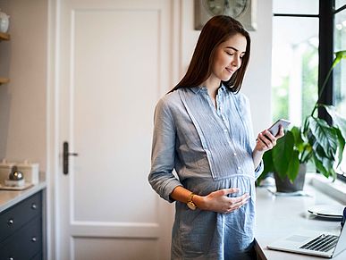 Schwangere Frau schaut auf ihr Smartphone