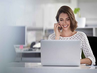 Frau sitzt vor einem Laptop und telefoniert