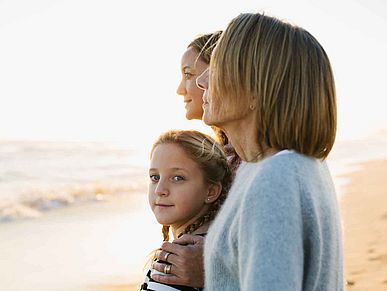 Frauen stehen mit einem Kind am Strand und schauen auf das Meer