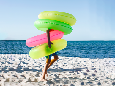 Mann am Strand trägt 4 aufblasbare Schwimmringe