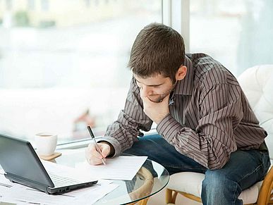 Mann sitzt vor seinem Laptop und macht Notizen