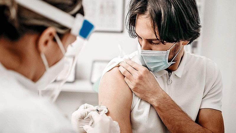 Eine Ärztin impft einen Mann. Beide tragen Masken.