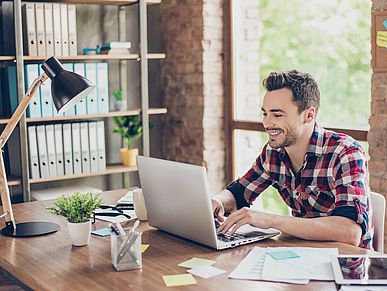 Junger Mensch sitzt an seinem Arbeitsplatz vor dem Laptop