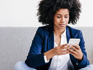 Frau sitzt auf dem Sofa und schaut auf ihr Smartphone