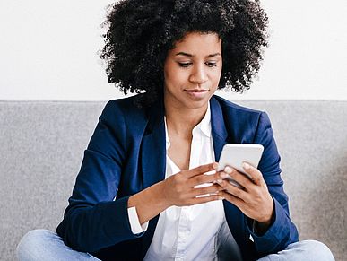 Frau sitzt auf dem Sofa und schaut auf ihr Smartphone