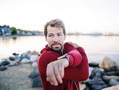 A fit mature sportsman runner doing exercise outdoors on beach, stretching