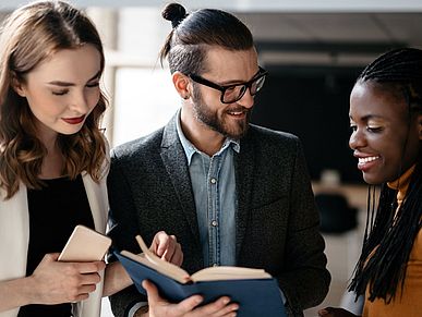 Eine Gruppe junger Erwachsener lehnen sich über ein Buch und besprechen sich